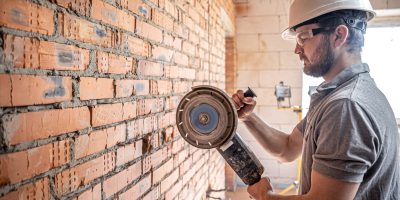 A professional builder in work clothes works with a cutting tool.